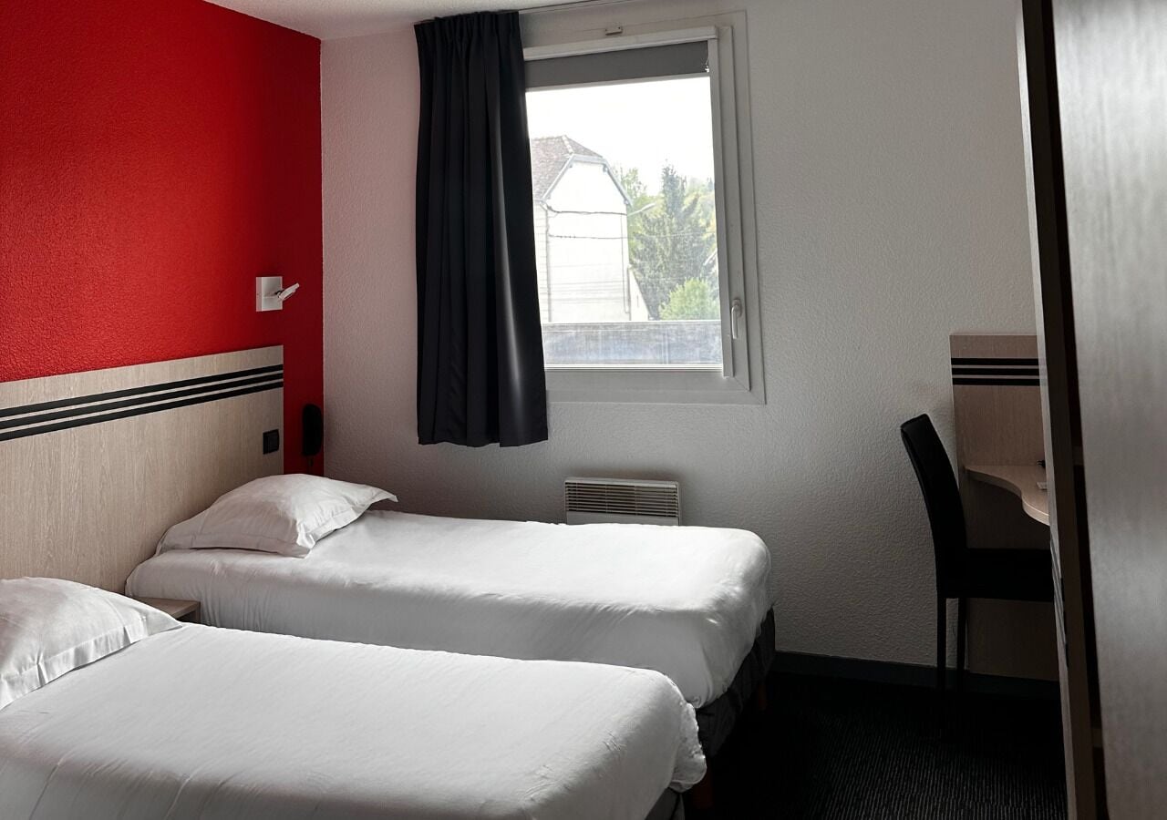 A hotel room with two beds, a window with a view, a desk, and a chair.