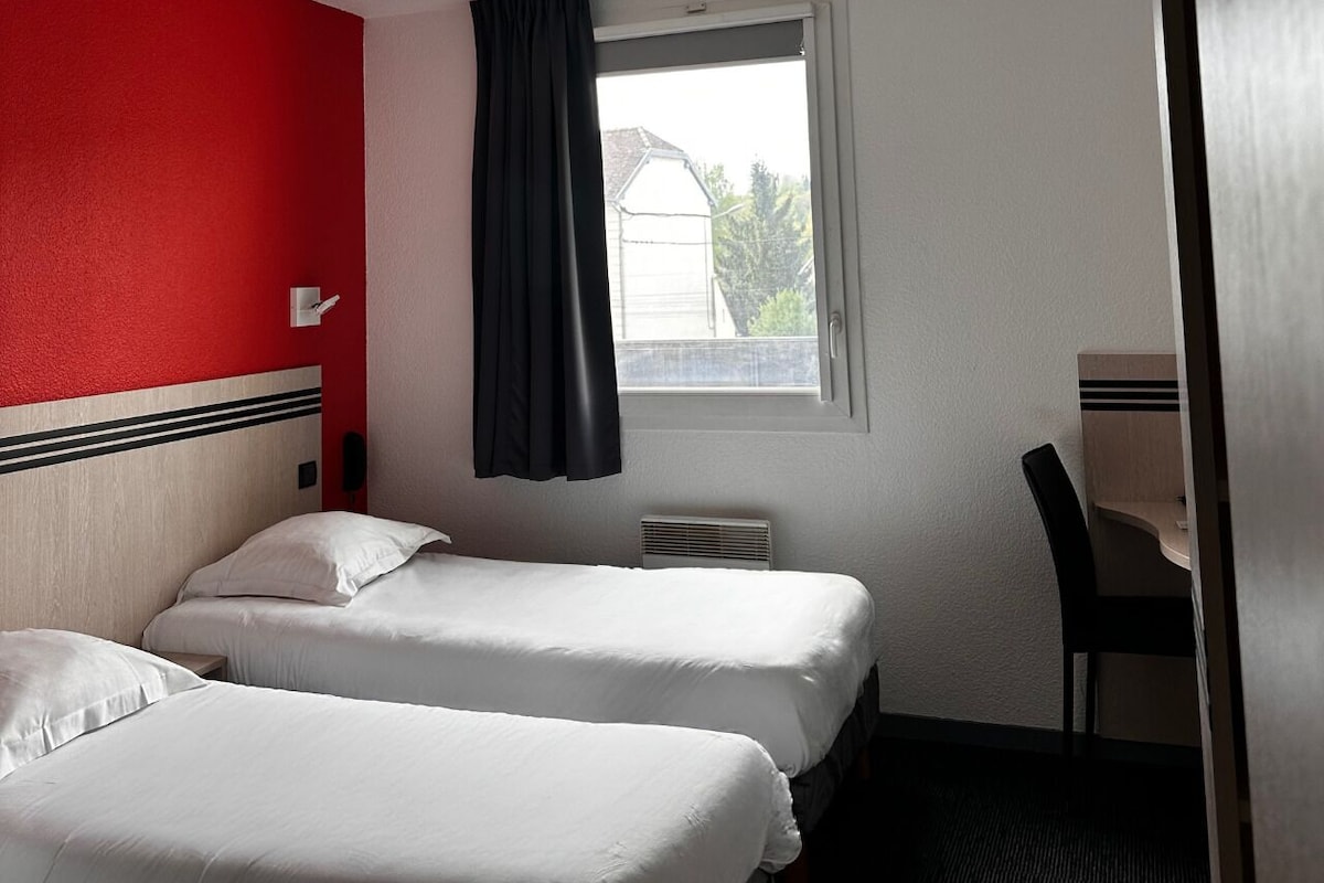 A hotel room with two beds, a window with a view, a desk, and a chair.