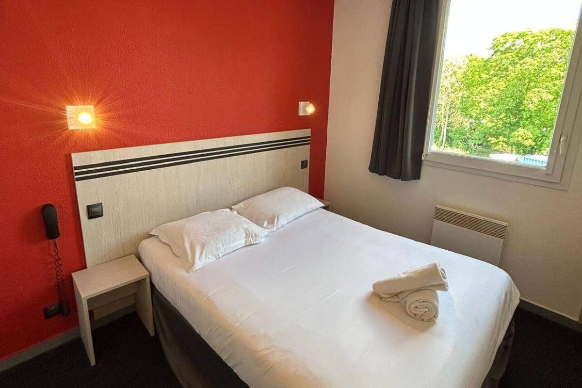 Une chambre d’hôtel avec un lit, une table de chevet, un téléphone et une fenêtre avec des rideaux.