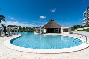 A swimming pool with a thatched-roof structure, lounge chairs, and a modern building in the background. - Beach Access, 4 Beds, 2 Bedroom, 2 Bath Quadrant 4107 (Bucerías)