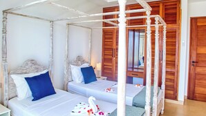 Een bed met hemelbed, voorzien van witte beddengoed en blauwe kussens, in een kamer met houten deuren en betegelde vloer.
