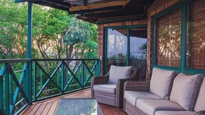 A covered outdoor seating area with wicker furniture and a glass table, surrounded by a wooden deck and green railings. - Cussonia Country Home (Tierpoort)
