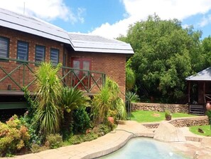 A brick building with a metal staircase, a swimming pool, and lush greenery. - Cussonia Country Home (Tierpoort)