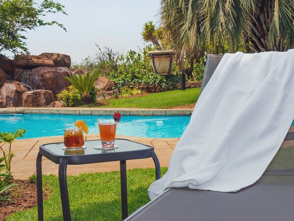 A poolside lounge chair with a white towel, a small table with two drinks, and a clear view of a pool and surrounding greenery. - Cussonia Country Home (Tierpoort)