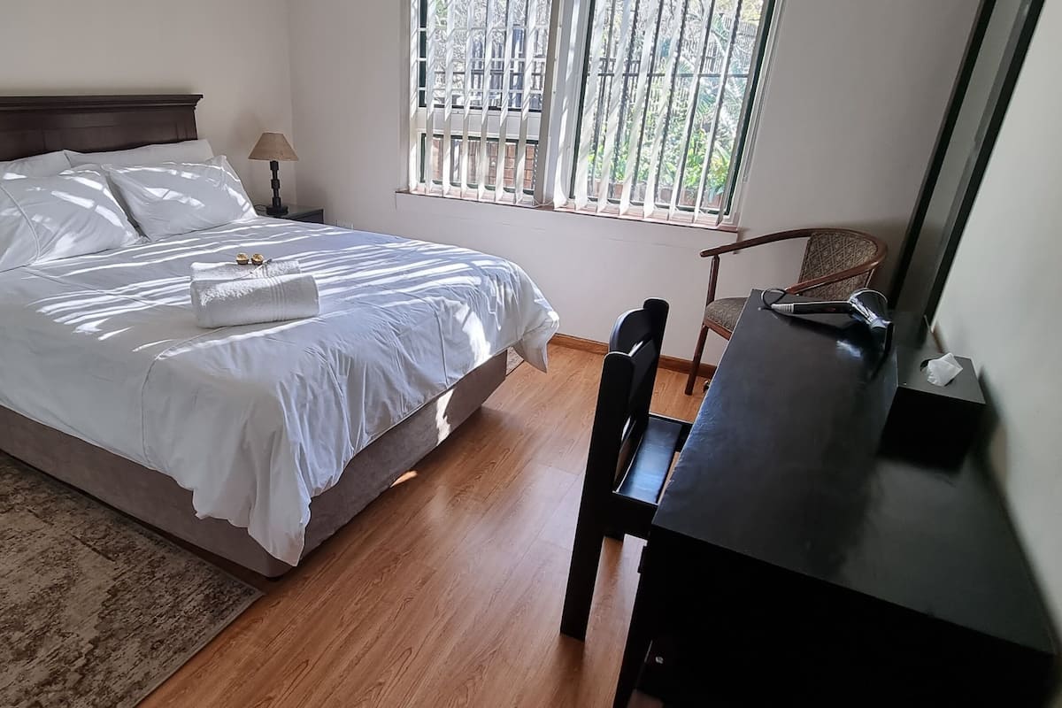 A neatly arranged bedroom with a bed, bedside tables, a desk, and a chair.