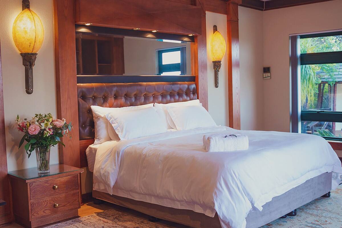 A neatly made bed with white linens, a wooden headboard, and two wall-mounted lamps.