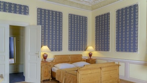 A bedroom with a wooden bed, two bedside tables with lamps, a wardrobe, and patterned wallpaper. - Hotel Heluan (Karlovy Vary)