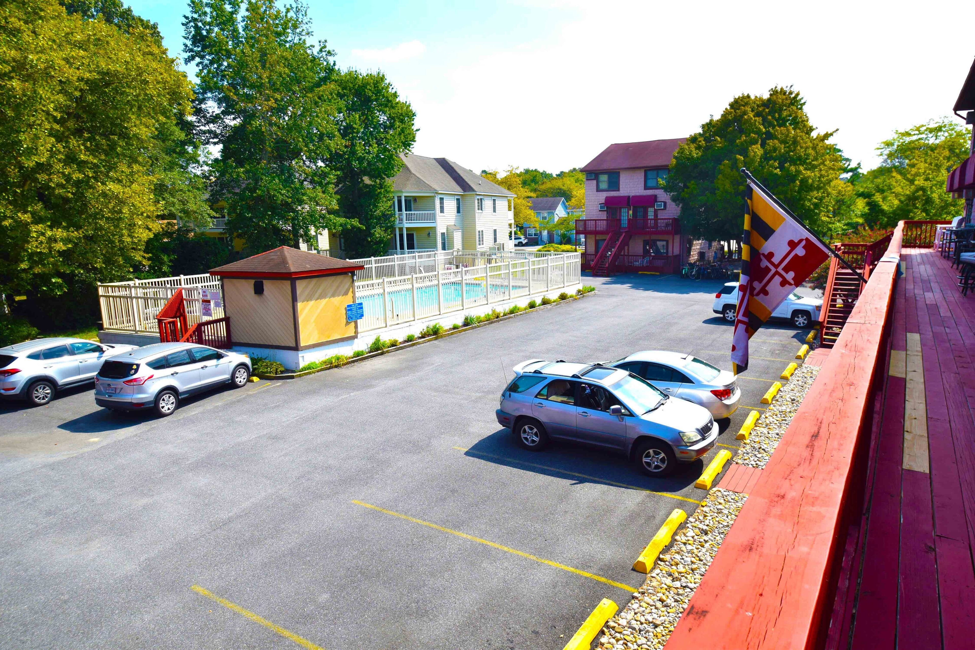 A parking lot with several cars, a small building with a red roof, and a flagpole with a flag.