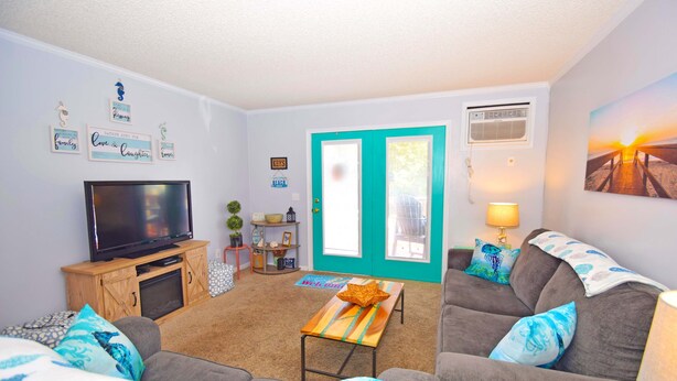 A living room with a television, sofa, and a teal door. - Nanticoke Square 207B-Bayside 142nd St, Pool, W/D, AC, Free WIFI (Ocean City)