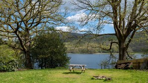 Una mesa de picnic junto a un lago, con árboles y una valla de madera.