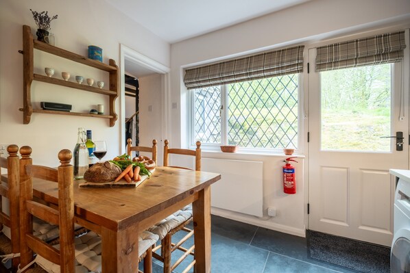A kitchen with a wooden table, chairs, a window with a view, and a fire extinguisher on the wall. - Potter's Wheel - sleeps 4, private lake access, dog friendly and parking (Coniston)