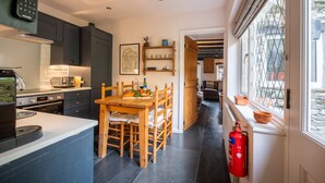 Una cocina moderna con armarios oscuros, una mesa de comedor de madera y un extintor cerca de la ventana.