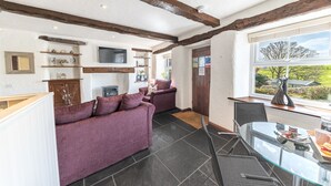 A cozy living room with a purple sofa, a glass table, and a TV mounted on the wall. - Mill Cottage - sleeps 2, dog friendly, peaceful with parking (Windermere)
