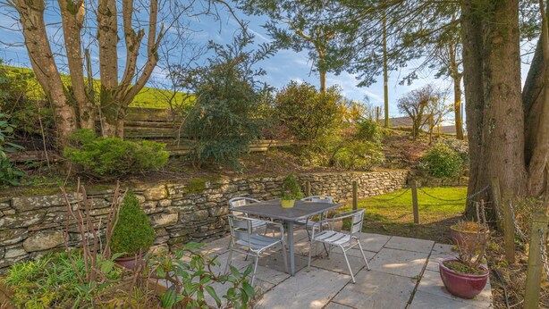 A patio with a table and chairs, surrounded by stone walls and various plants. - Mill Cottage - sleeps 2, dog friendly, peaceful with parking (Windermere)