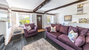 A modern living room with a purple sofa set, a fireplace, and a view of the outdoors. - Mill Cottage - sleeps 2, dog friendly, peaceful with parking (Windermere)