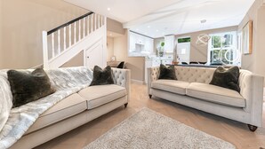 A spacious living area with two sofas, a staircase, and a kitchen in the background. - Heather Mere Cottage - sleeps 4 in newly renovated property (Bowness-on-Windermere)