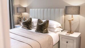 A neatly made bed with a tufted headboard, two bedside lamps, and a bedside table with a lamp. - Heather Mere Cottage - sleeps 4 in newly renovated property (Bowness-on-Windermere)
