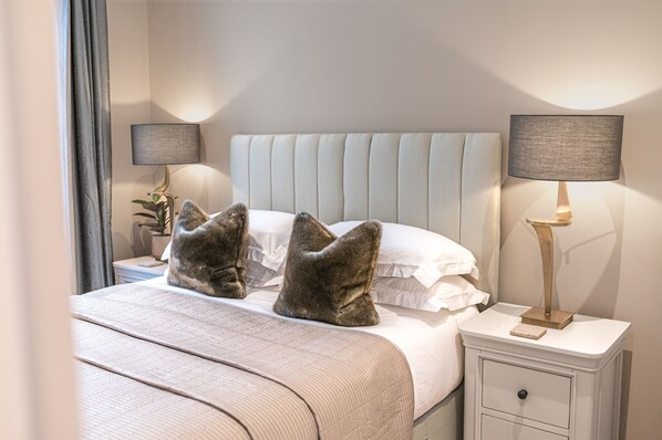 A neatly made bed with a tufted headboard, two bedside lamps, and a bedside table with a lamp.