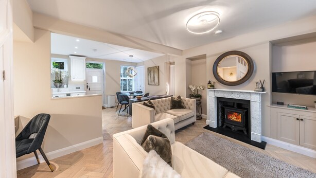 A spacious living room with a fireplace, a dining area, and a kitchen visible through an open door. - Heather Mere Cottage - sleeps 4 in newly renovated property (Bowness-on-Windermere)