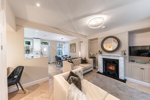 A spacious living room with a fireplace, a dining area, and a kitchen visible through an open door.