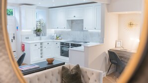 A modern kitchen with white cabinetry, a central island, and a dining area with a sofa and a table. - Heather Mere Cottage - sleeps 4 in newly renovated property (Bowness-on-Windermere)