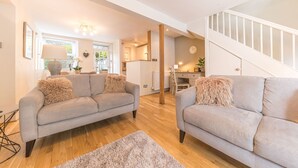 A modern living room with two grey sofas, a wooden floor, a staircase, and a dining area with a table and chairs. - Pottery Gate - sleeps 4 in modern dog friendly cottage with parking and new bathroom (Bowness-on-Windermere)