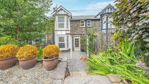 A stone house with a stone facade, a front door, and a small garden with potted plants and a pathway. - Pottery Gate - sleeps 4 in modern dog friendly cottage with parking and new bathroom (Bowness-on-Windermere)