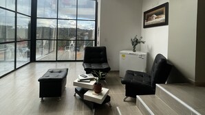 A spacious room with large windows, a black leather sofa, a small table with a plant, and a painting on the wall. - Beautiful villa overlooking the forest + jacuzzi (Guarne)
