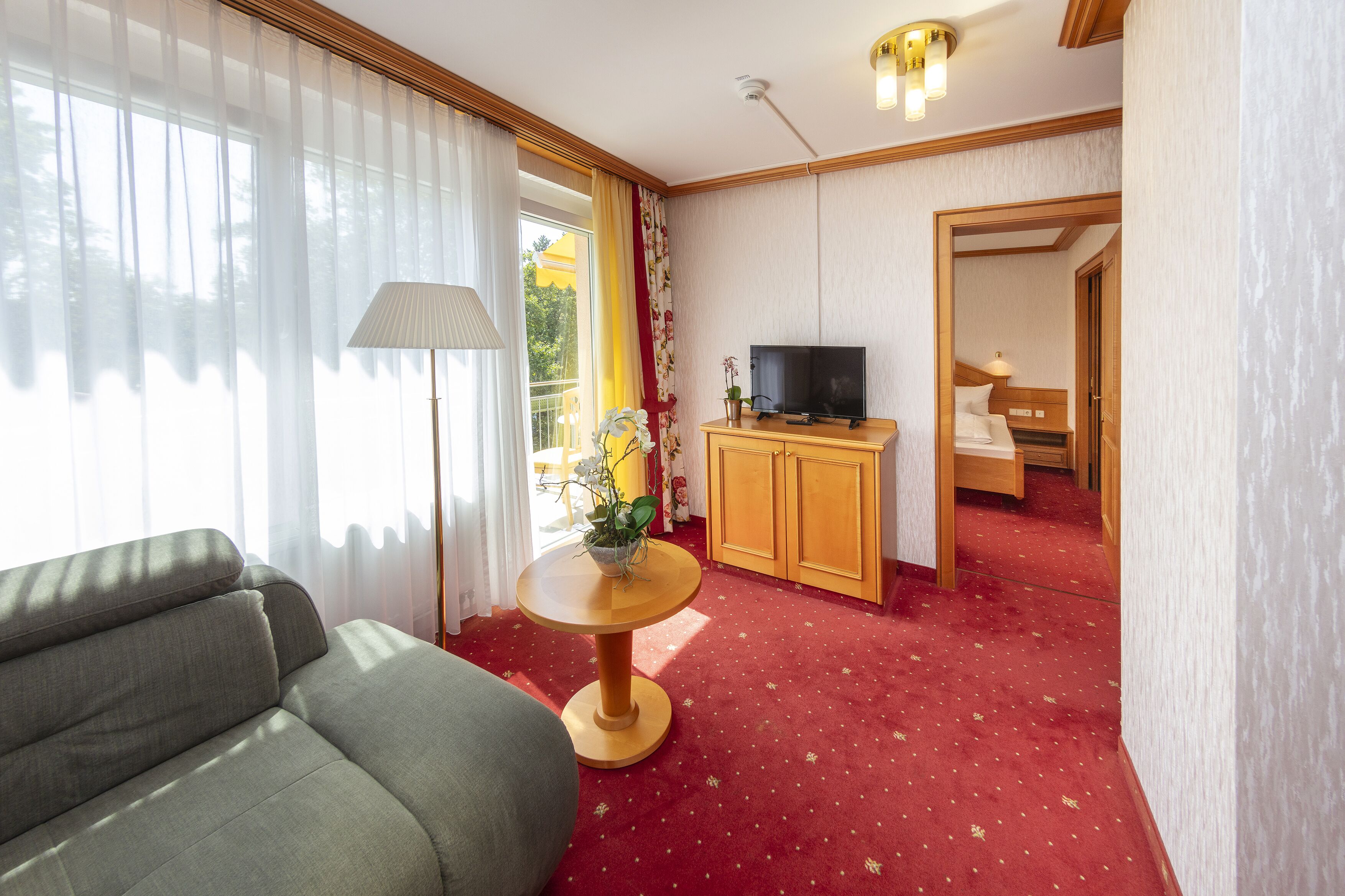 Habitación de hotel con sofá, una mesita redonda con lámpara, televisor y mueble de madera.