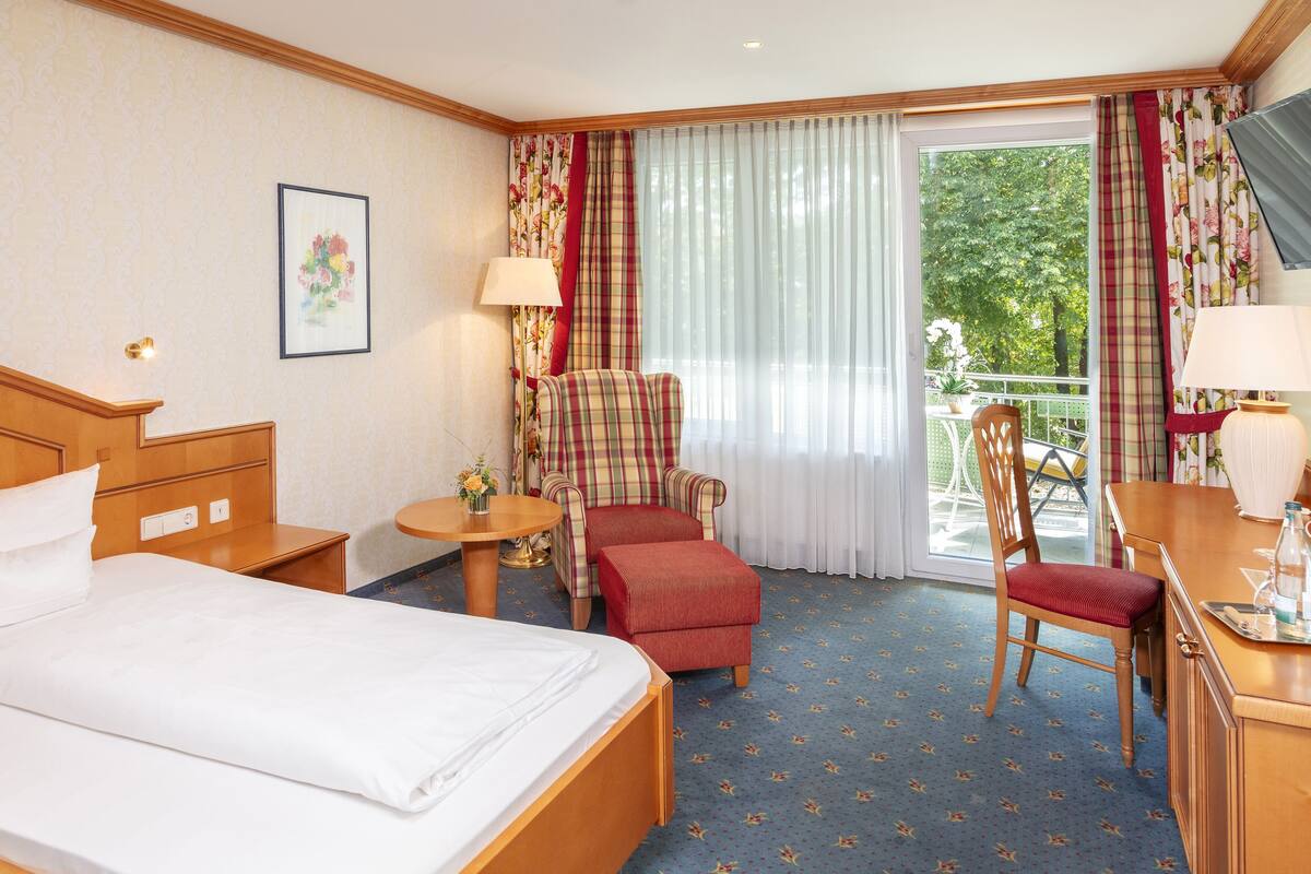 Une chambre d’hôtel avec un lit, une chaise, une petite table et un balcon donnant sur la verdure.