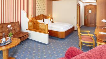 A hotel room with a bed, a wooden headboard, a sofa, a chair, a small table, and a decorative plant.