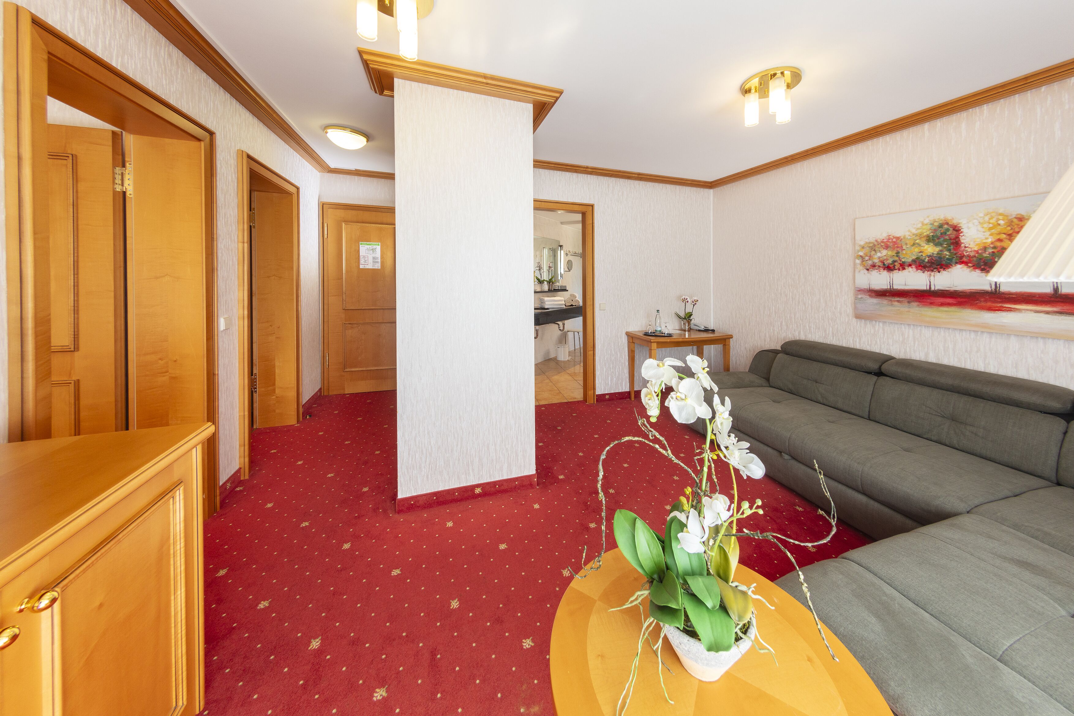 Une chambre d’hôtel avec une moquette rouge, un canapé, une armoire en bois et un tableau accroché au mur.