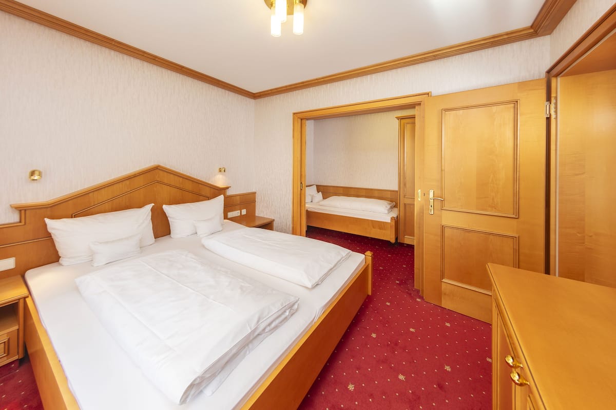 Une chambre d’hôtel avec un grand lit, un lit plus petit, des meubles en bois et une moquette rouge.