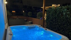 Ett bubbelbad med blått ljus, omgivet av växter och ett trädäck.