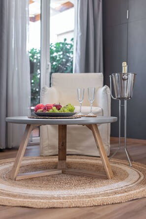 A round table with a woven placemat, a bowl of fruit, and two glasses on a rug.