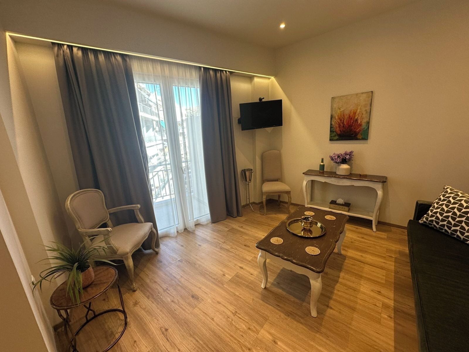 A living room with a TV, a dining table, a sofa, a chair, a small side table, and a plant.