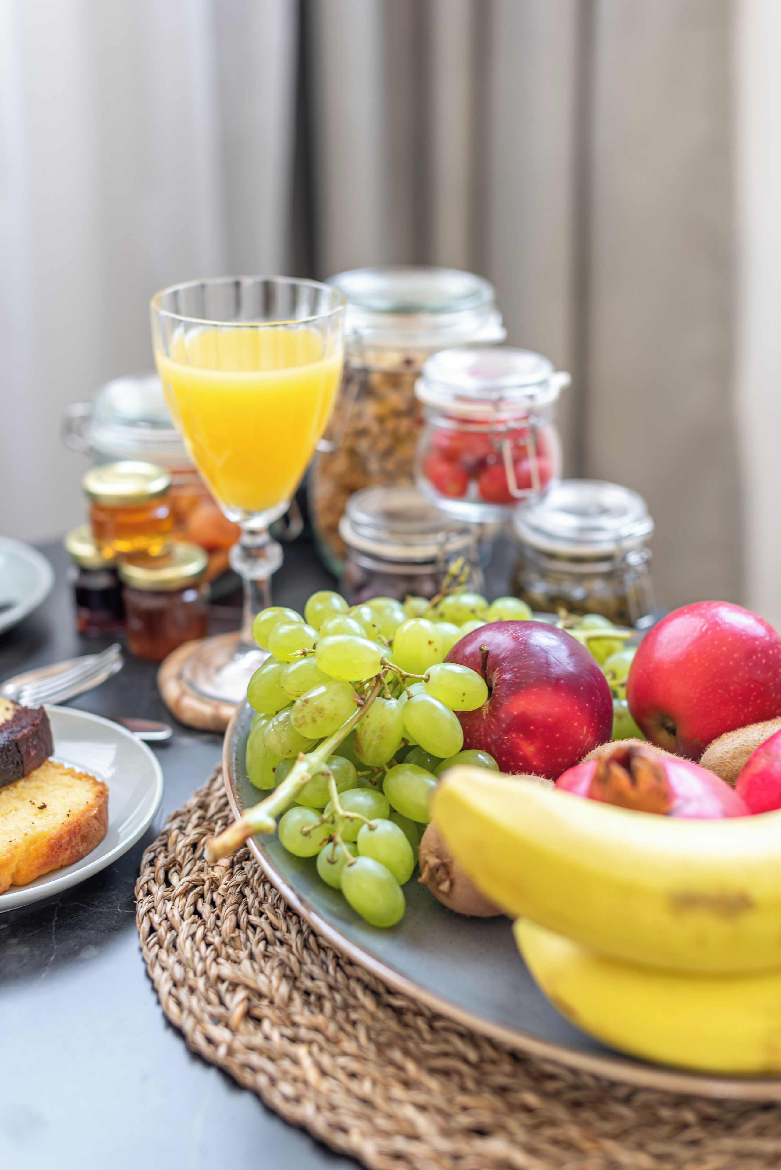 En frukostuppsättning med frukt, ett glas apelsinjuice och burkar med sylt.