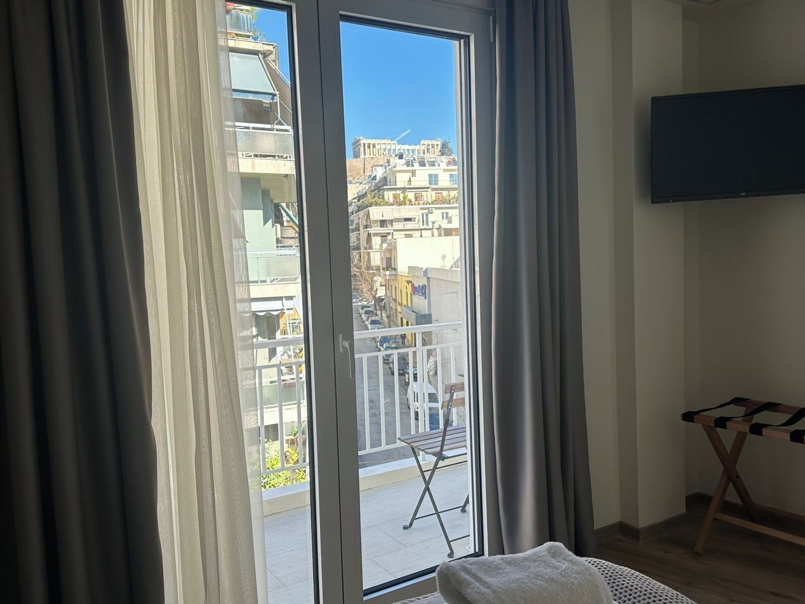 Una habitación con puerta de vidrio corredera a un balcón exterior, un televisor de pantalla plana montado en la pared y un banco de madera.
