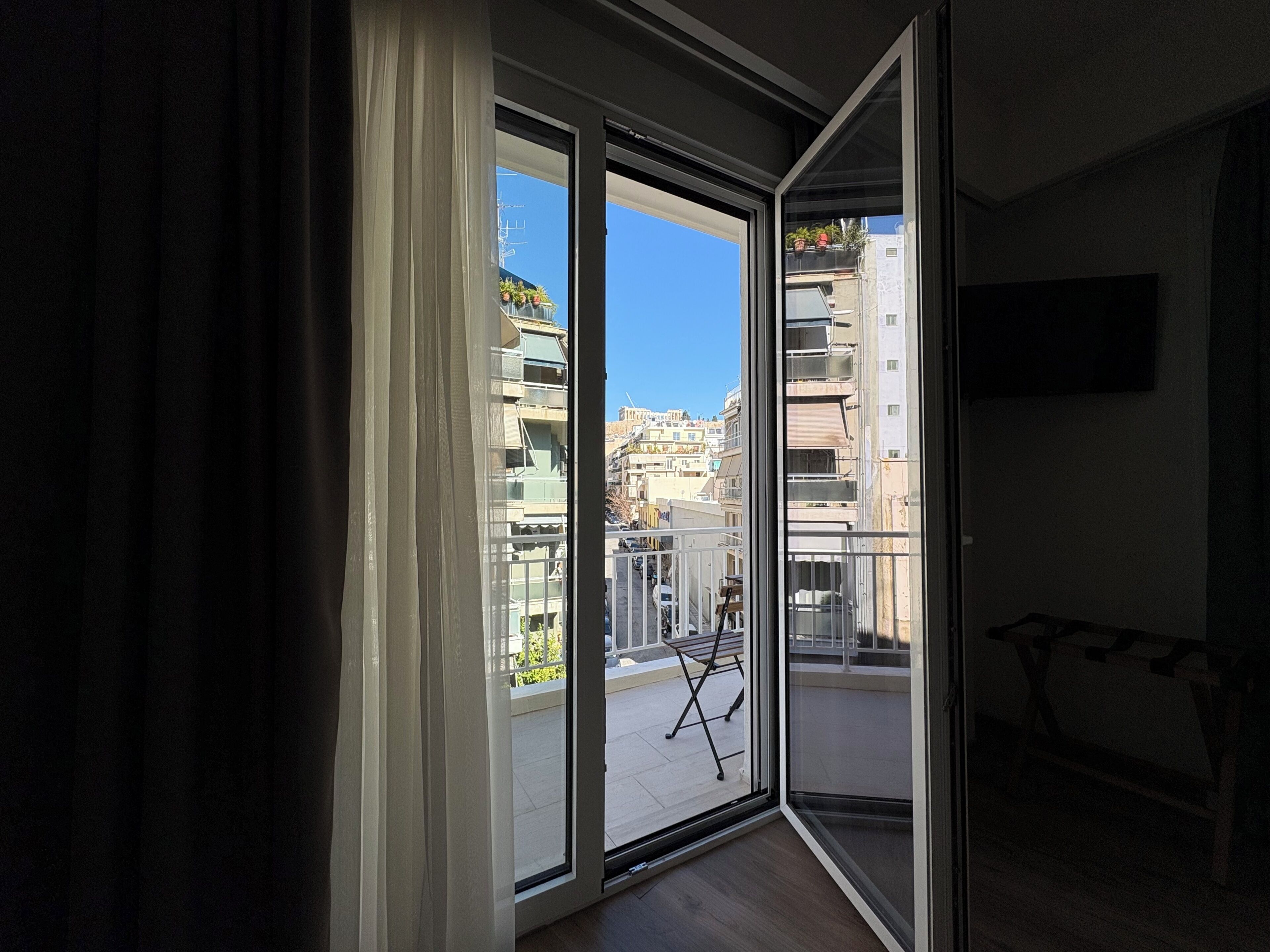 A room with a large sliding glass door leading to an outdoor balcony with a view of buildings and a clear sky.