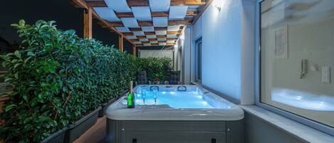 A hot tub with a wooden pergola overhead, potted plants, and a window with a view.