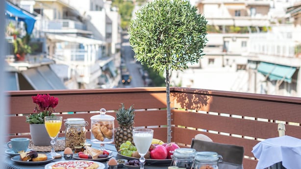 En balkong med ett bord dukat för frukost, med utsikt över stadsbilden.