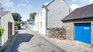 En smal gata kantad av traditionella byggnader i sten och puts, en stenmur med en blomlåda och en blå dörr med skylten "Privat parkering".