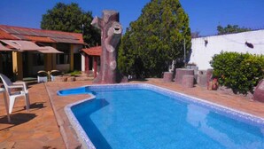 A swimming pool with a tree-shaped structure in the center, surrounded by a patio area with chairs and a building in the background. - Pousada Caldas Novas (Caldas Novas)