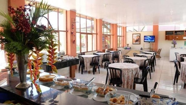 A dining area with tables and chairs, a buffet with food items, and a television on the wall. - Pousada Caldas Novas (Caldas Novas)