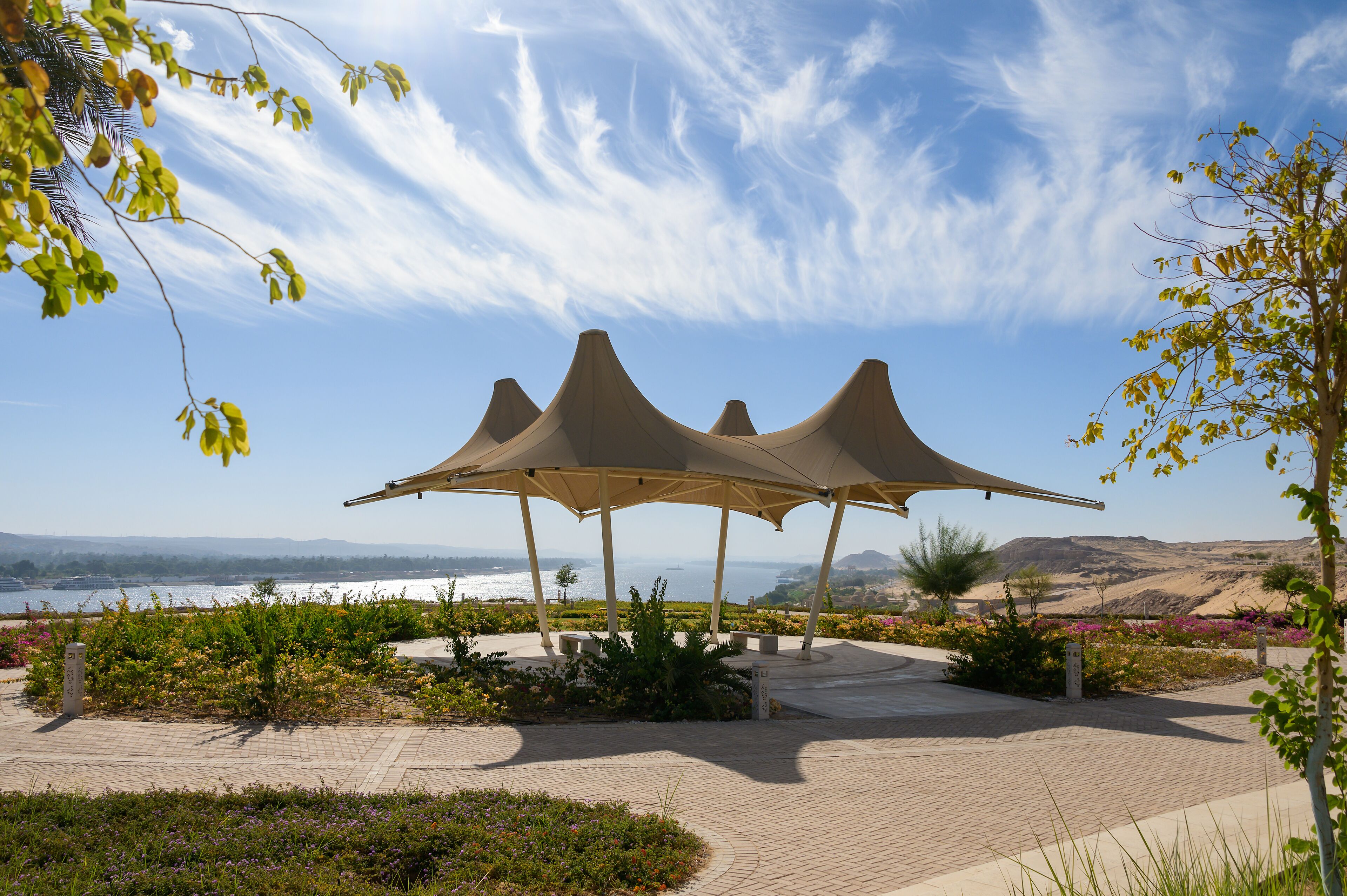 Un pabellón con una estructura de techo singular, rodeado de jardines ajardinados y vistas al mar.