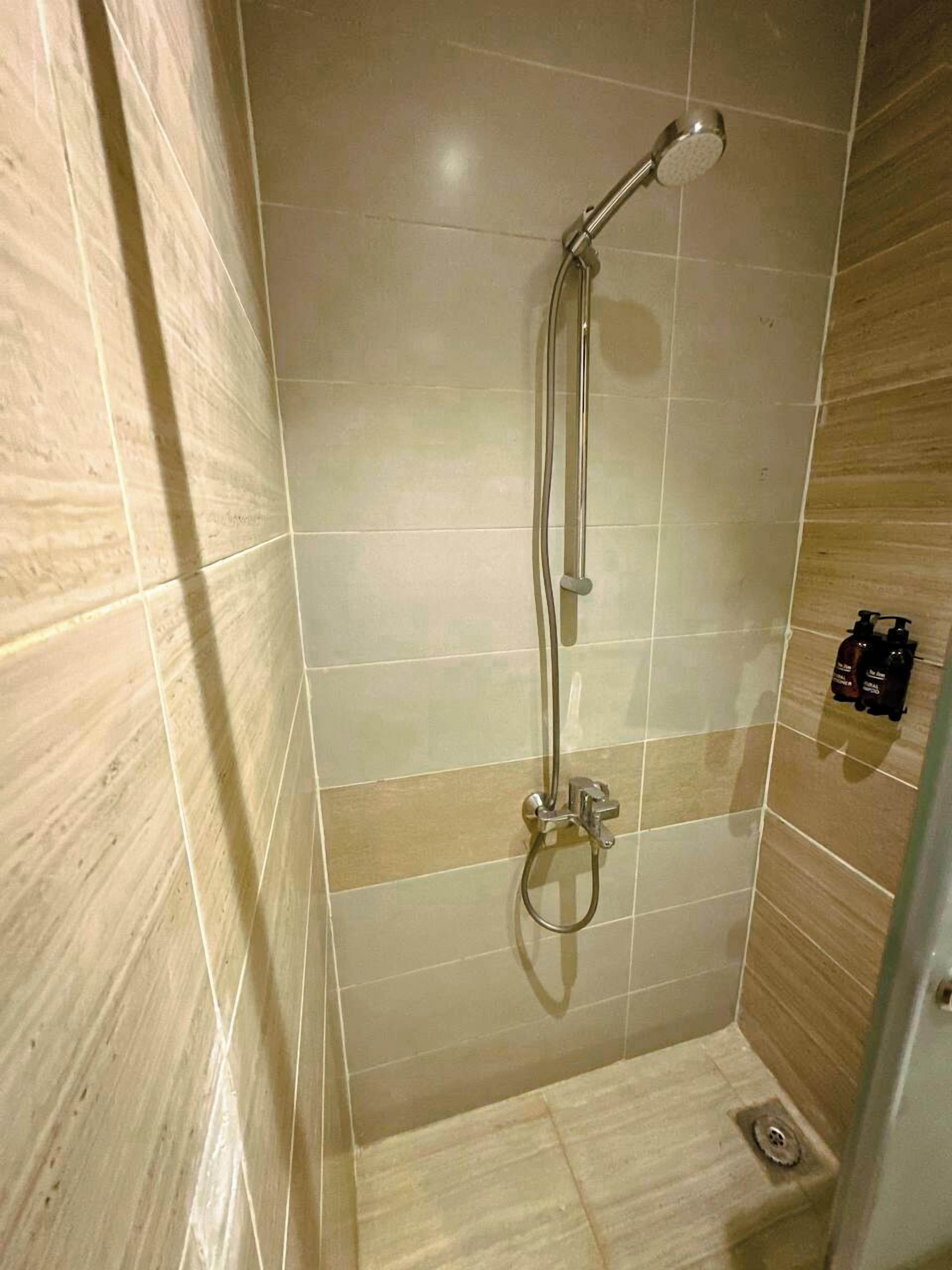 A shower with a handheld showerhead and a wall-mounted faucet.