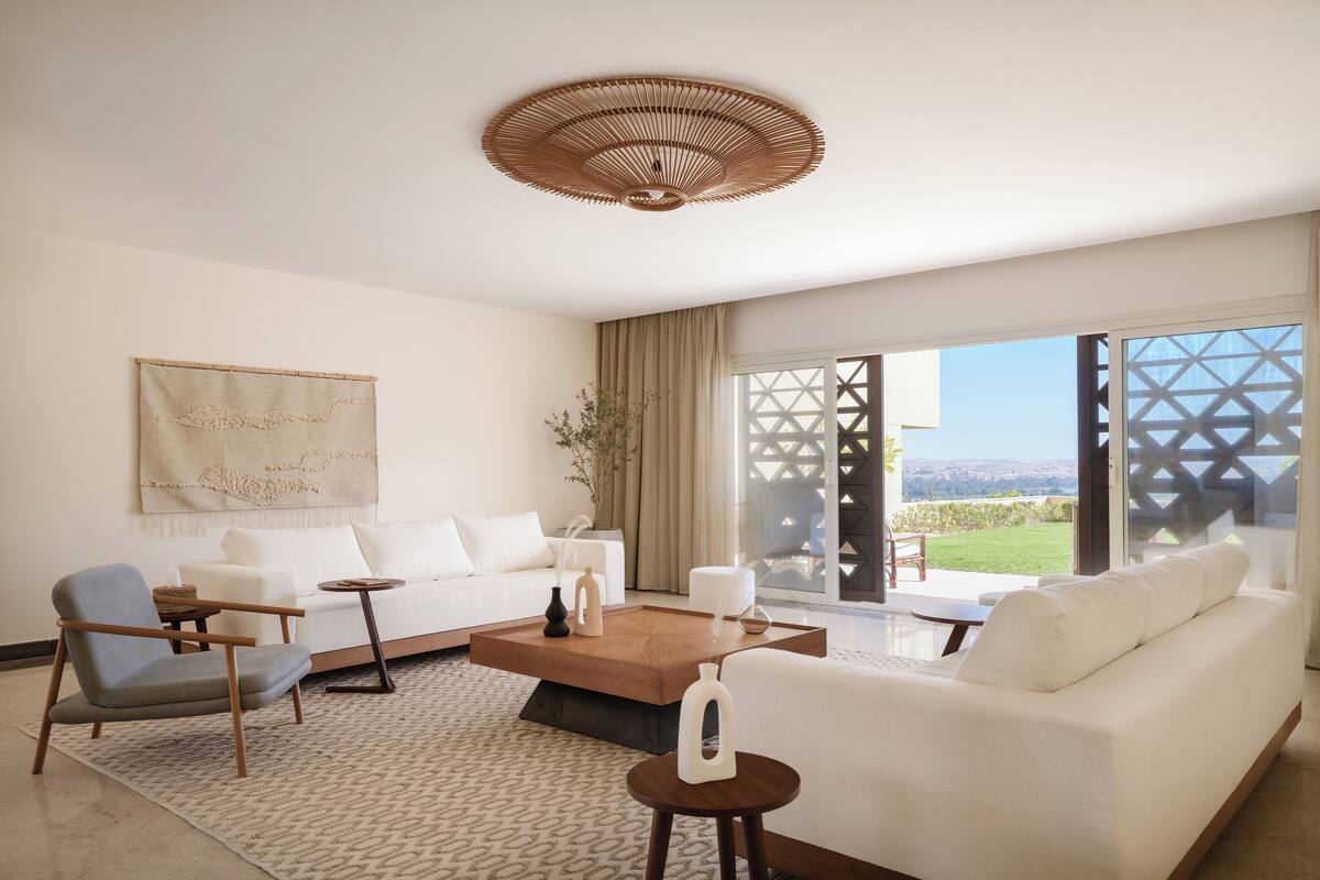 A modern living room with a sofa, armchairs, a coffee table, and a large window offering a view of the outdoors.