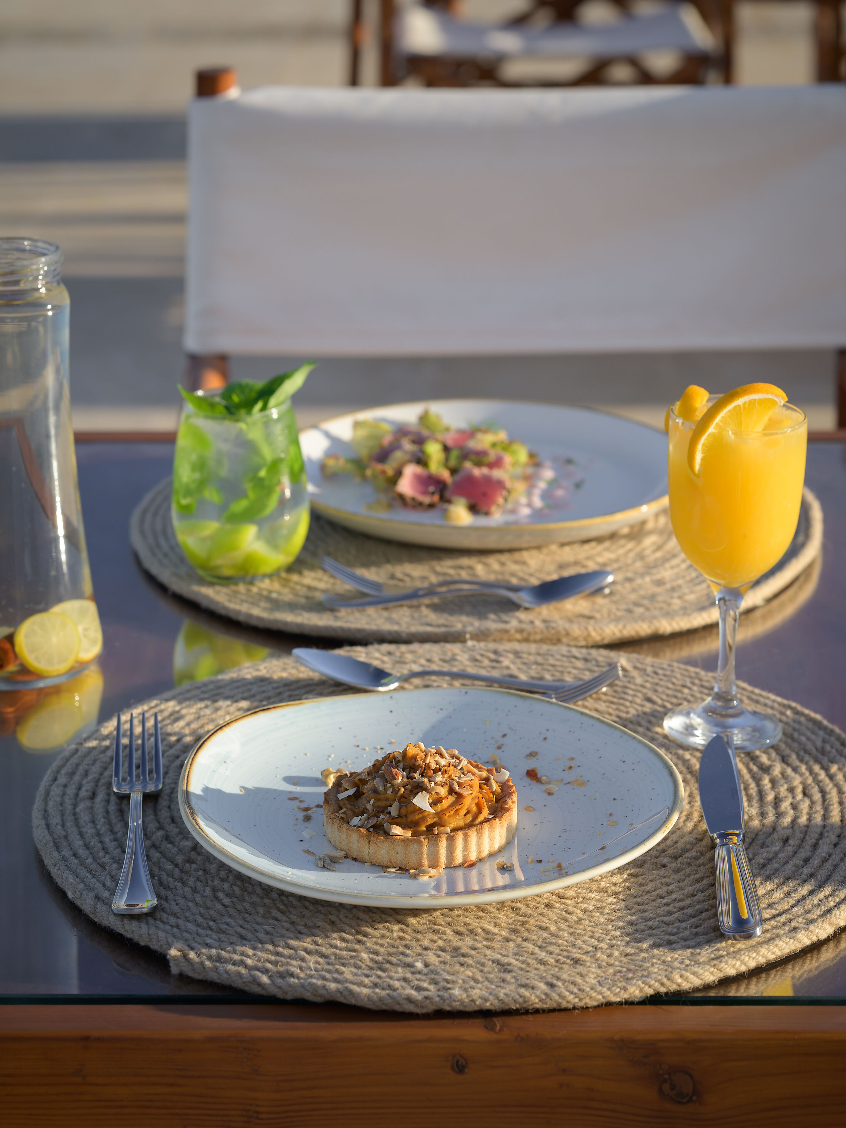 A table set with plates of food, cutlery, and a glass of orange juice.
