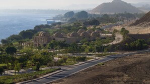 Vista costera con una carretera que lleva a un edificio histórico con estructuras abovedadas.