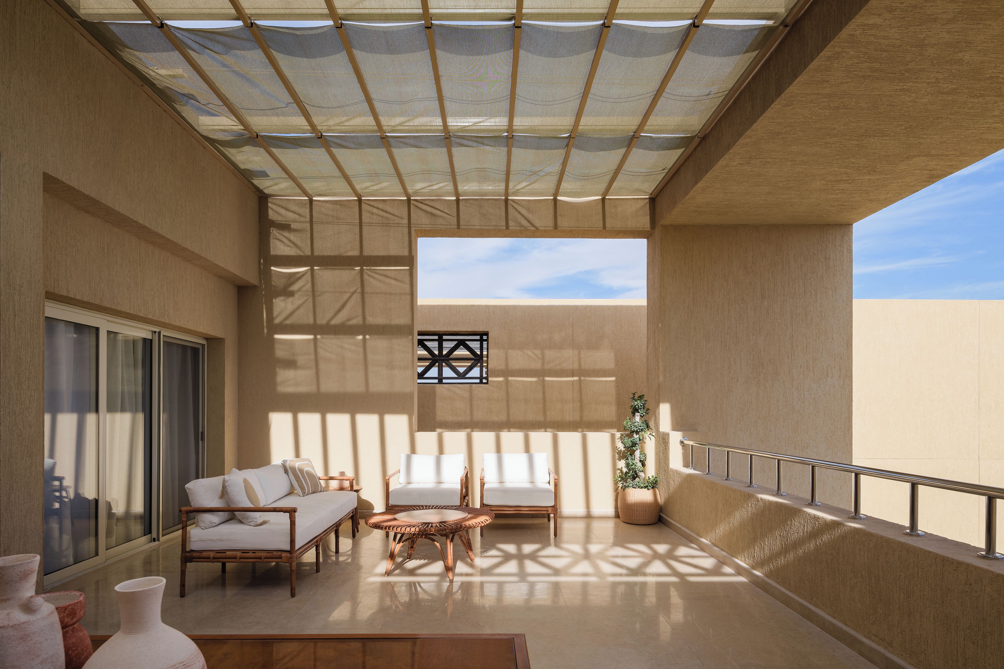 A spacious balcony with a sunshade, two white sofas, a round wooden table, and a potted plant.